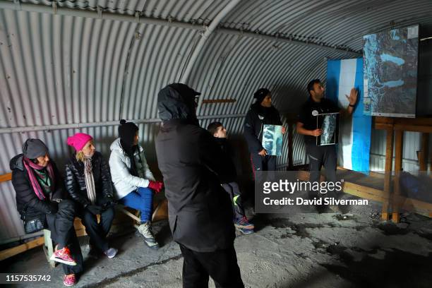 An Argentinian guide describes to tourists in a glacial research station quonset hut how the Upsala glacier has receded in the past 90 years during...