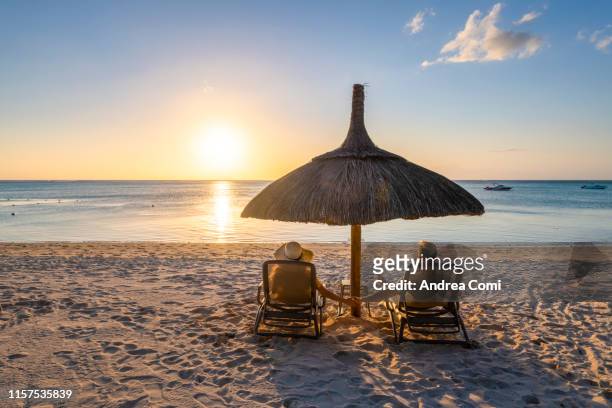a young couple holding hands admires the sunset in a tropical beach - beach holiday stock-fotos und bilder