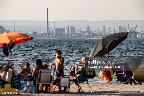 People enjoy the beach in front of the steel manufacturing giant Arcelor Mittal Italia plant, in Taranto, southern Italy, on July 22, 2019. - The...