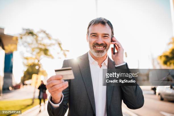 mann telefoniert und hält kreditkarte - anzug ausland stock-fotos und bilder