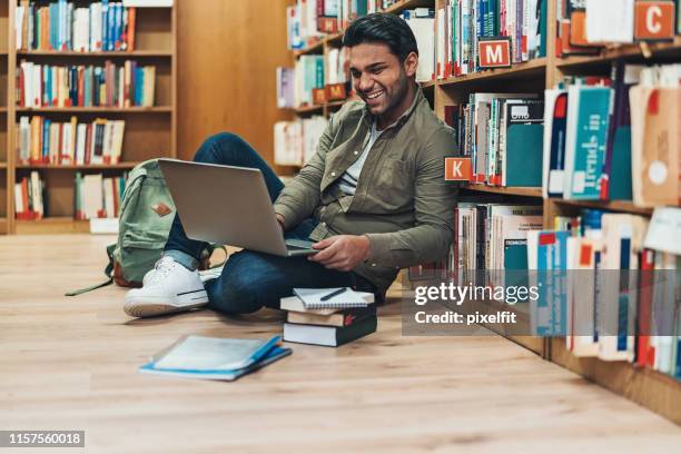 student with laptop sitting on the floor in a library - arabic literature stock pictures, royalty-free photos & images