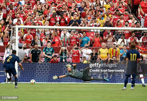 Fans behind the goal take photos and videos with their phones while Real Madrid goalie Thibaut Courtois dives in vain to stop a Arsenal goal during...