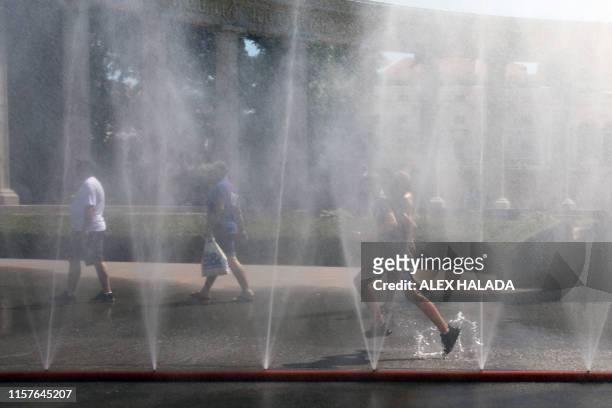 People run through water sprayed from a pipe at the Schwarzenberg square in front of the monument of the Red Army in Vienna on July 25, 2019. Weather...