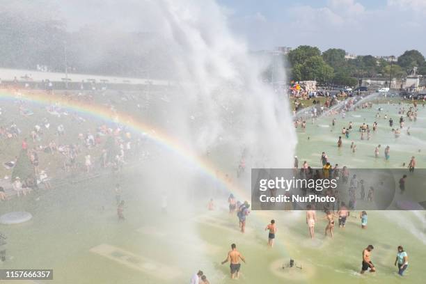 Many Parisians and tourists cool down under the powerful jet of water from the trocadero fountain which has formed a rainbow as Paris and all of...