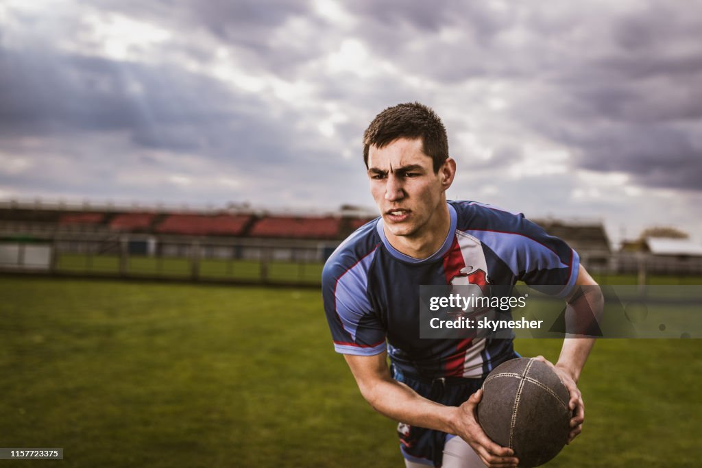 Sportif déterminé courant avec le bille sur le terrain de rugby.