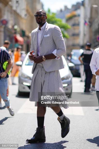 Basket-ball player Serge Ibaka wears a striped blazer jacket, a white shirt, a watch, pleated skirt, sunglasses, outside Thom Browne, during Paris...