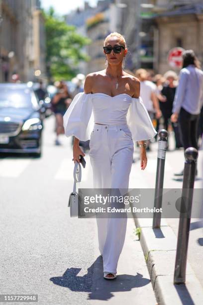 Elina Halimi wears sunglasses, an off-shoulder flared top, flared pants, a bag, outside Thom Browne, during Paris Fashion Week - Menswear...