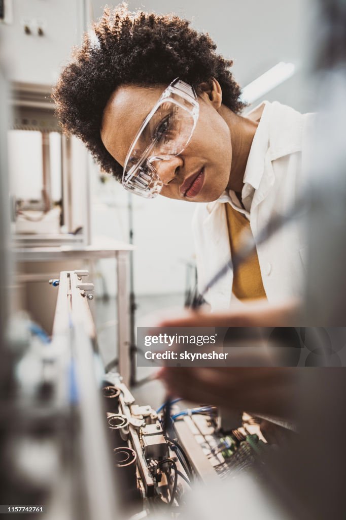 Black female engineer working on industrial machine in a laboratory.