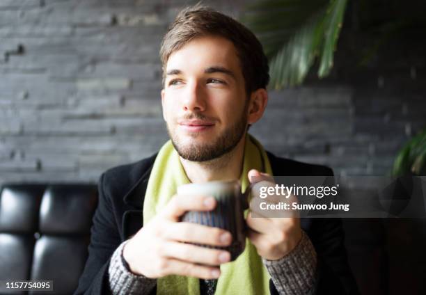 portrait of young man in cafe holding mug - iris mann stock-fotos und bilder