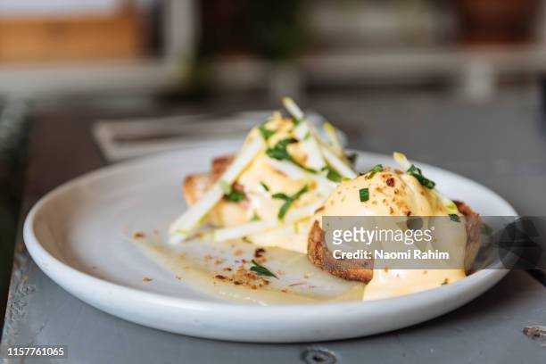 poached eggs covered in hollandaise sauce on toasted bread, served on a table for brunch - melbourne food imagens e fotografias de stock