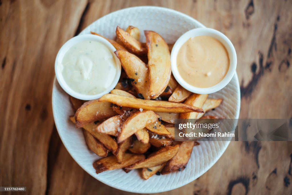 Gourmet potato wedges served with black sea salt & aioli in a white bowl, shot directly above