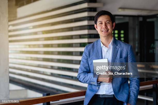 retrato del hombre de negocios asiático con tableta digital al aire libre sobre el edificio de oficinas en segundo plano - thai ethnicity fotografías e imágenes de stock