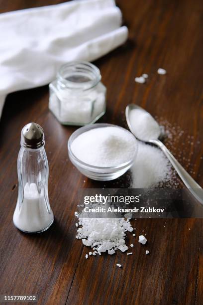 natural seasoning, organic, sea, small and large, white salt in a spoon, in a cup, in a salt shaker, poured on a wooden table. next to a linen towel. the concept of cooking healthy food, cosmetology. - zout smaakstof stockfoto's en -beelden