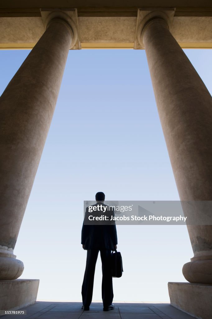 Businessman Standing Between Columns