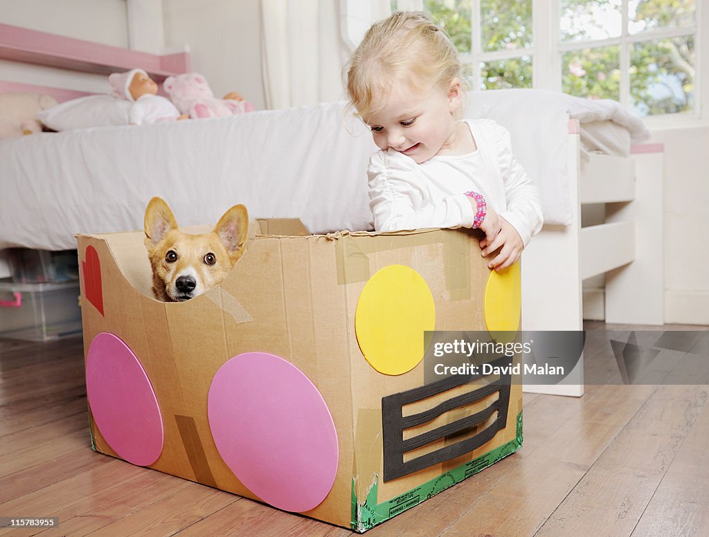 Girl in cardboard box car with her dog.