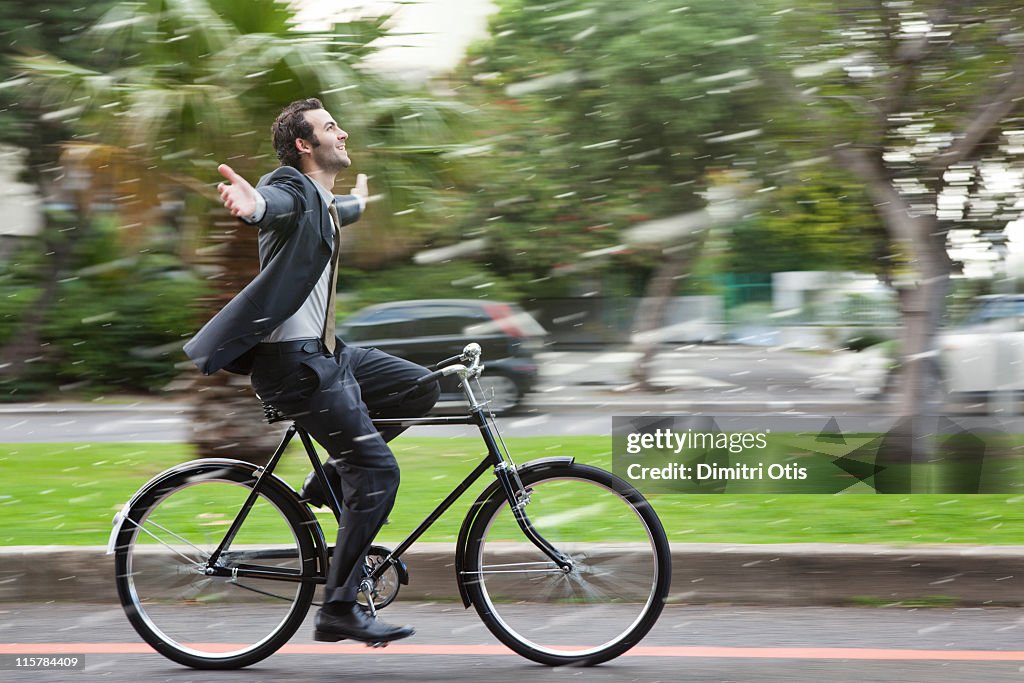 Businessman cycling in the rain, hands in the air