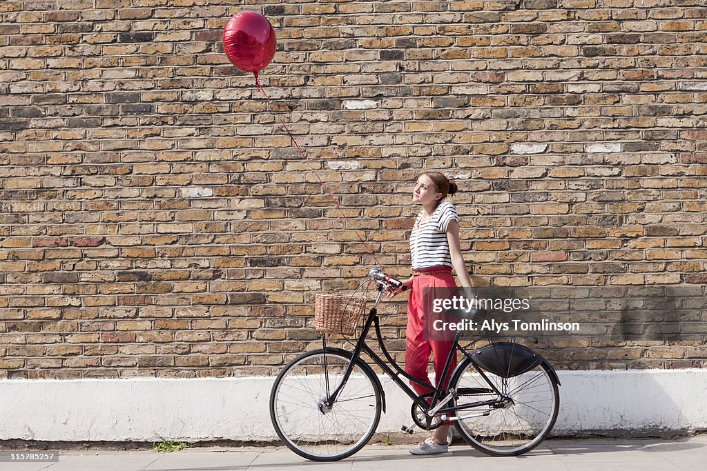 Young woman against wall with bike and balloon