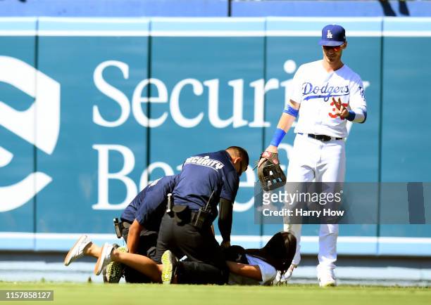 Cody Bellinger of the Los Angeles Dodgers waves to a fan as she is handcuffed by security for running onto the field during the ninth inning against...