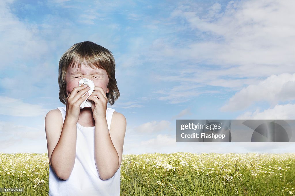 Boy surrounded by flowers sneezing into a tissue