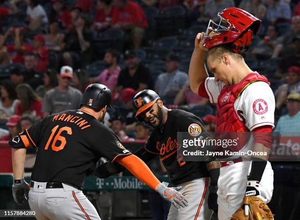 Dustin Garneau of the Los Angeles Angels looks on as Trey Mancini is greeted by Jonathan Villar of the Baltimore Orioles after hitting a two run home...