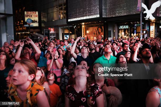 People watch as Nik Wallenda and Lijana Wallenda cross Times Square on a high wire strung between two skyscrapers 25 stories above the pavement on...