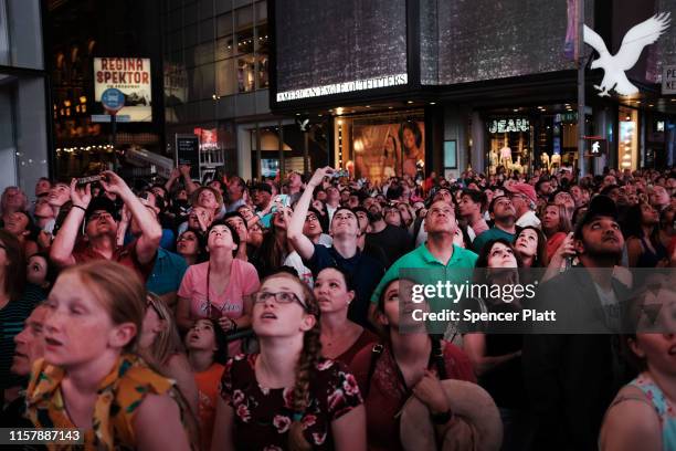 People watch as Nik Wallenda and Lijana Wallenda cross Times Square on a high wire strung between two skyscrapers 25 stories above the pavement on...