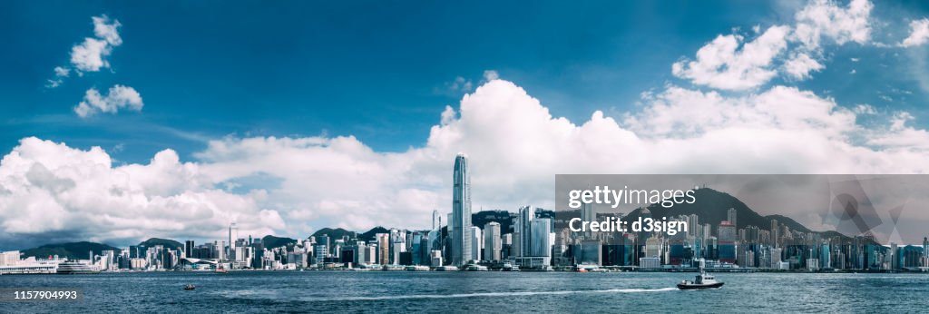 Panoramic view of iconic Hong Kong city skyline with Victoria Harbour against clear blue sky