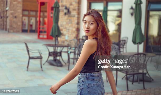 young asian woman walking down street looking over shoulder - looking over shoulder photos et images de collection
