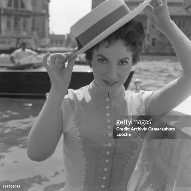 Italian actress Gina Lollobrigida wearing an embroidered dress and a straw hat, portrayed in a close-up, the Canal Grande behind her, Venice, 1954.