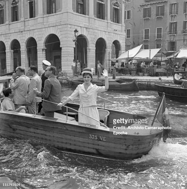 Italian actress Gina Lollobrigida wearing a tailleur, gloves and a bowler hat, greeting from a water taxi passing in front of the Rialto market,...