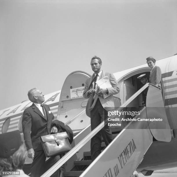 American actor Paul Newman, holding papers and sunglasses, getting down the stairs of an Alitalia airplane in Tessera airport, Marco Polo, a hostess...