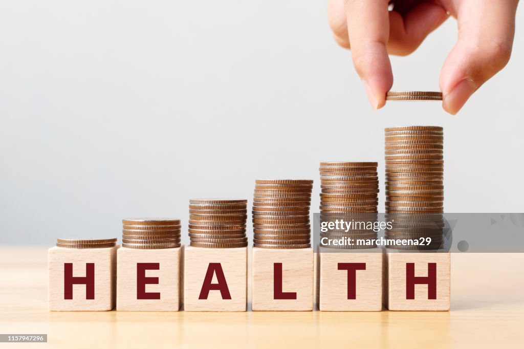 Hand putting coins on stack stair as step growing growth and wooden cube block with word HEALTH. Investment health and insurance fund concept