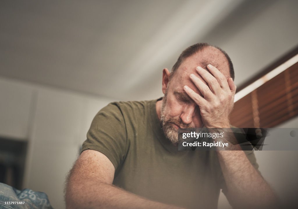 Tired and despairing mature man in his bedroom in the morning