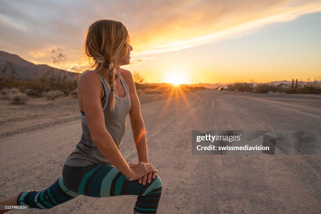 Junge Frau streckt Körper nach dem Joggen, Sonnenuntergang am Ende der Straße; Weibchen dehnt Körper in der Natur