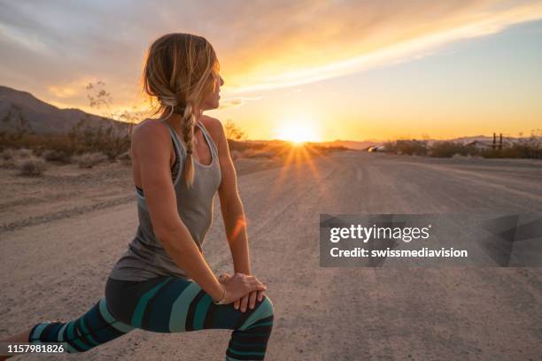 jonge vrouw stretching lichaam na het joggen, zonsondergang aan het einde van de weg; vrouwelijke stretches lichaam in de natuur - yoga outdoor stockfoto's en -beelden