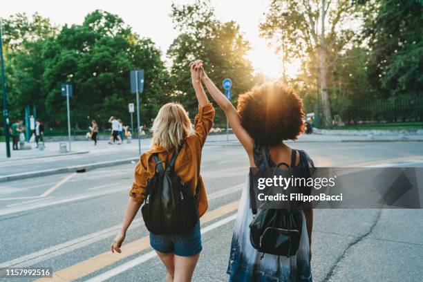 two friends walking together in the city at sunset - open arms hug stock pictures, royalty-free photos & images