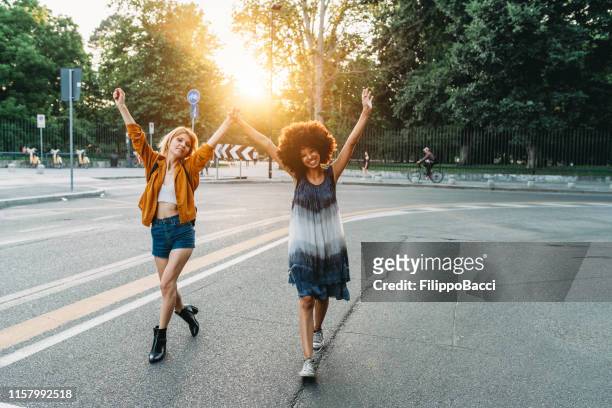 zwei freunde, die bei sonnenuntergang gemeinsam in der stadt spazieren gehen - frauenpower stock-fotos und bilder