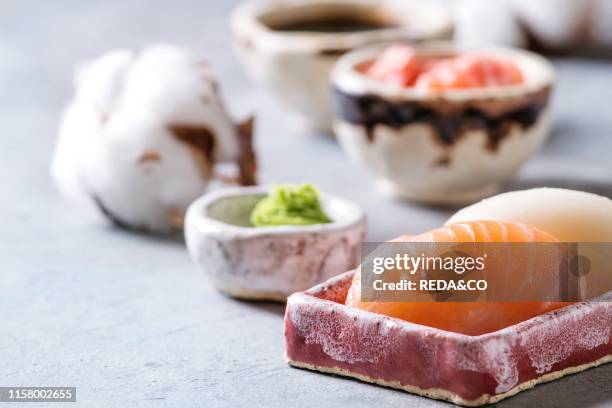 Sushi Set nigiri with salmon and butterfish in pink ceramic serving plate with bowls of soy sauce and pickled ginger. Cotton flowers on light blue...