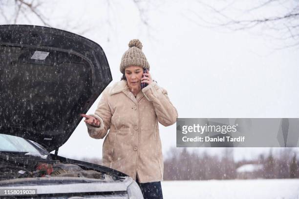 woman using mobile phone beside broken down car. - winter panne auto stock-fotos und bilder