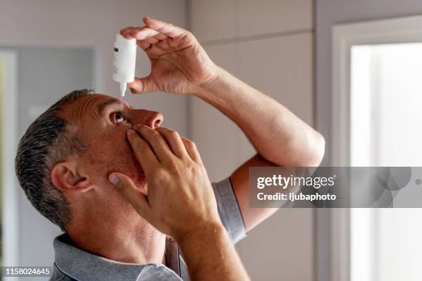 mature man putting eye drops in eyes - colírio imagens e fotografias de stock