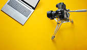 Online concept blogger, reviewer. Camera on tripod, laptop on yellow background. Minimalism.