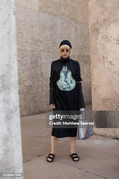 Guest is seen on the street during men's Paris Fashion Week wearing black graphic dress with black sandals and hat on June 22, 2019 in Paris, France.