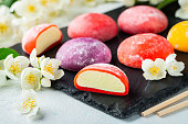 Multi-colored Japanese ice cream Mochi in rice dough and Jasmine flowers on a concrete blue background. Traditional Japanese dessert on a black slate