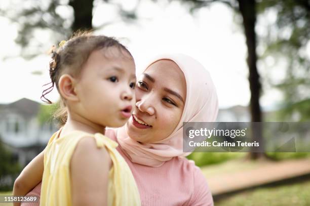 malay woman holding her young daughter in a park - malaysia family stock pictures, royalty-free photos & images