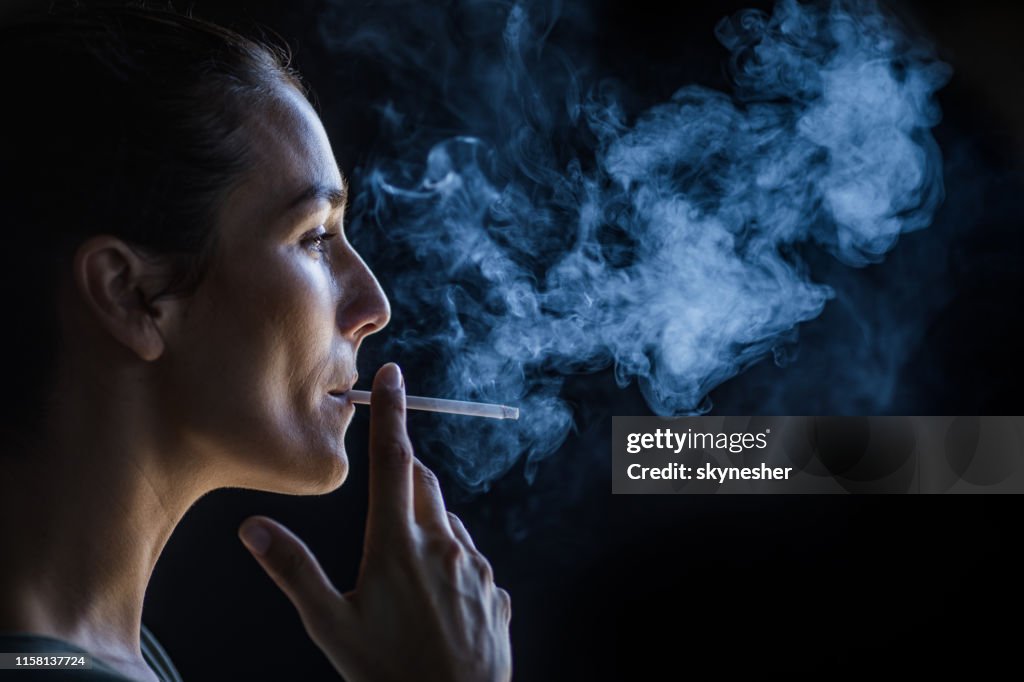 Profile view of beautiful woman smoking in the dark.