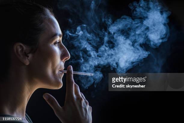 profile view of beautiful woman smoking in the dark. - smoking issues stock pictures, royalty-free photos & images