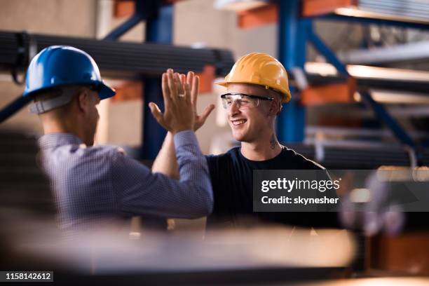 happy steel worker en zijn manager geven elkaar high-five in een magazijn. - hi five stockfoto's en -beelden