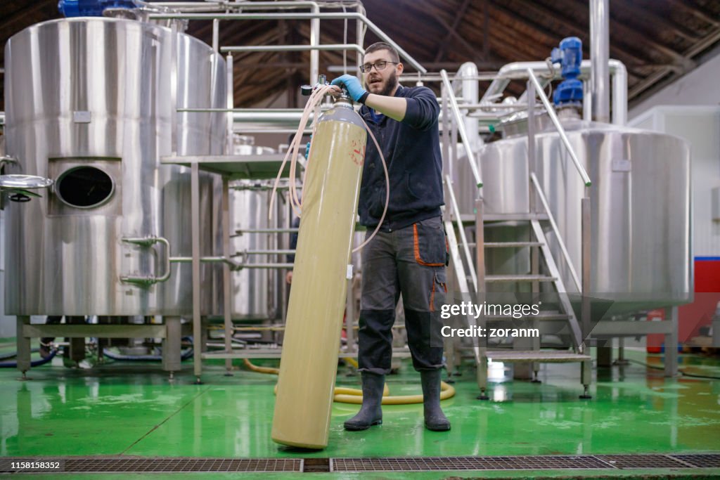 Worker in brewery holding tall oxygen tank