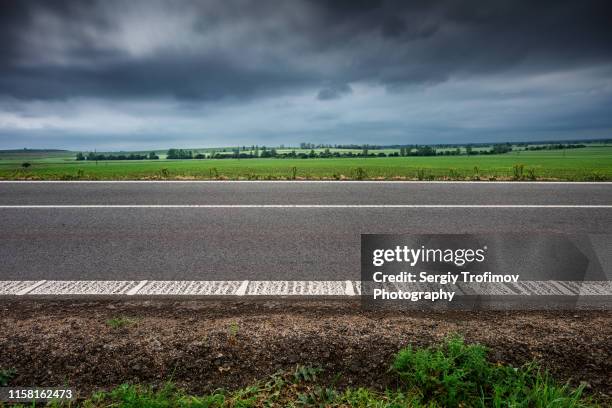 road along the field in rainy day side view - borde de la carretera fotografías e imágenes de stock
