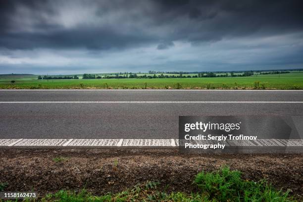 road along the field in rainy day side view - roadside stock pictures, royalty-free photos & images